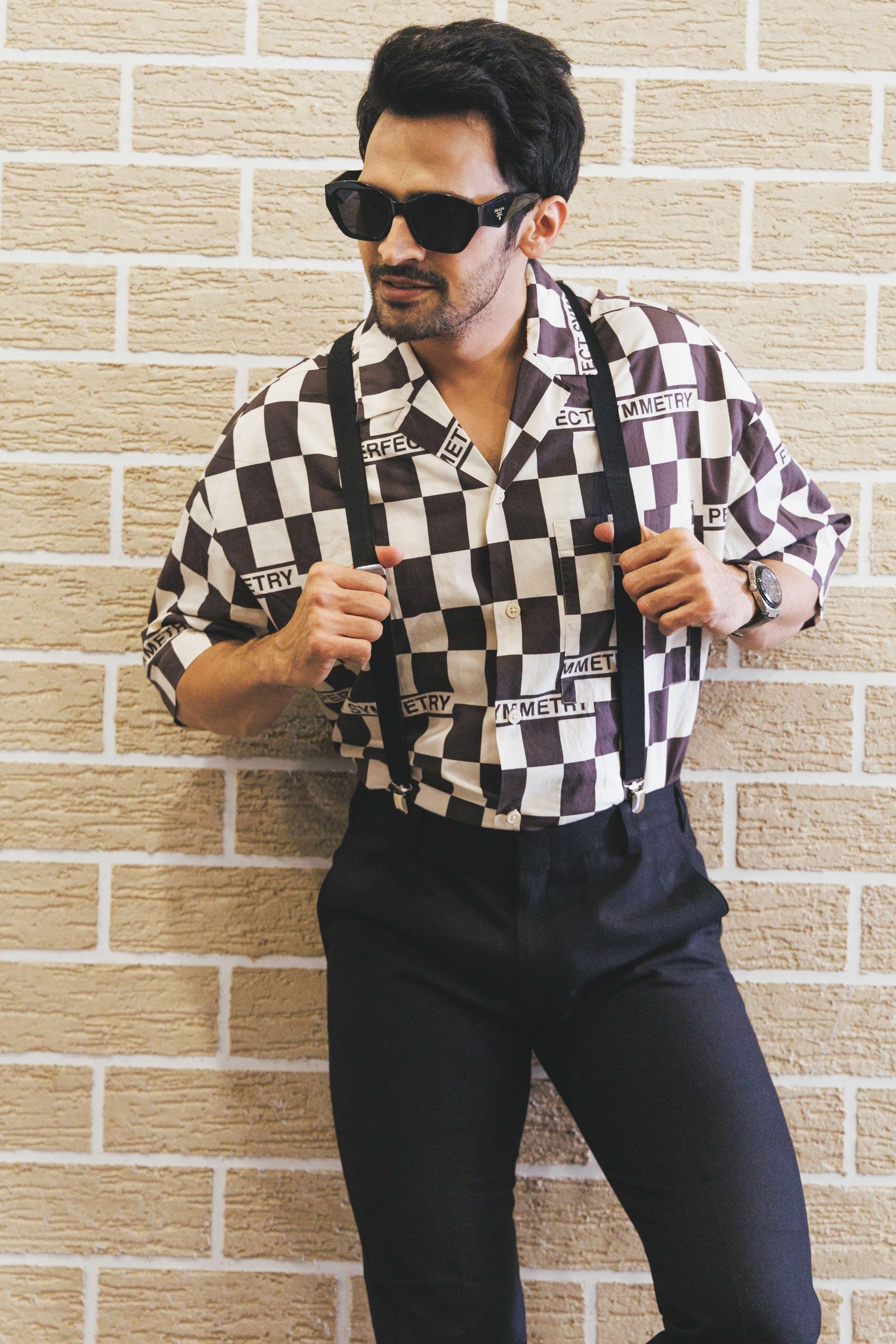Model in a checked shirt and sunglasses against brick