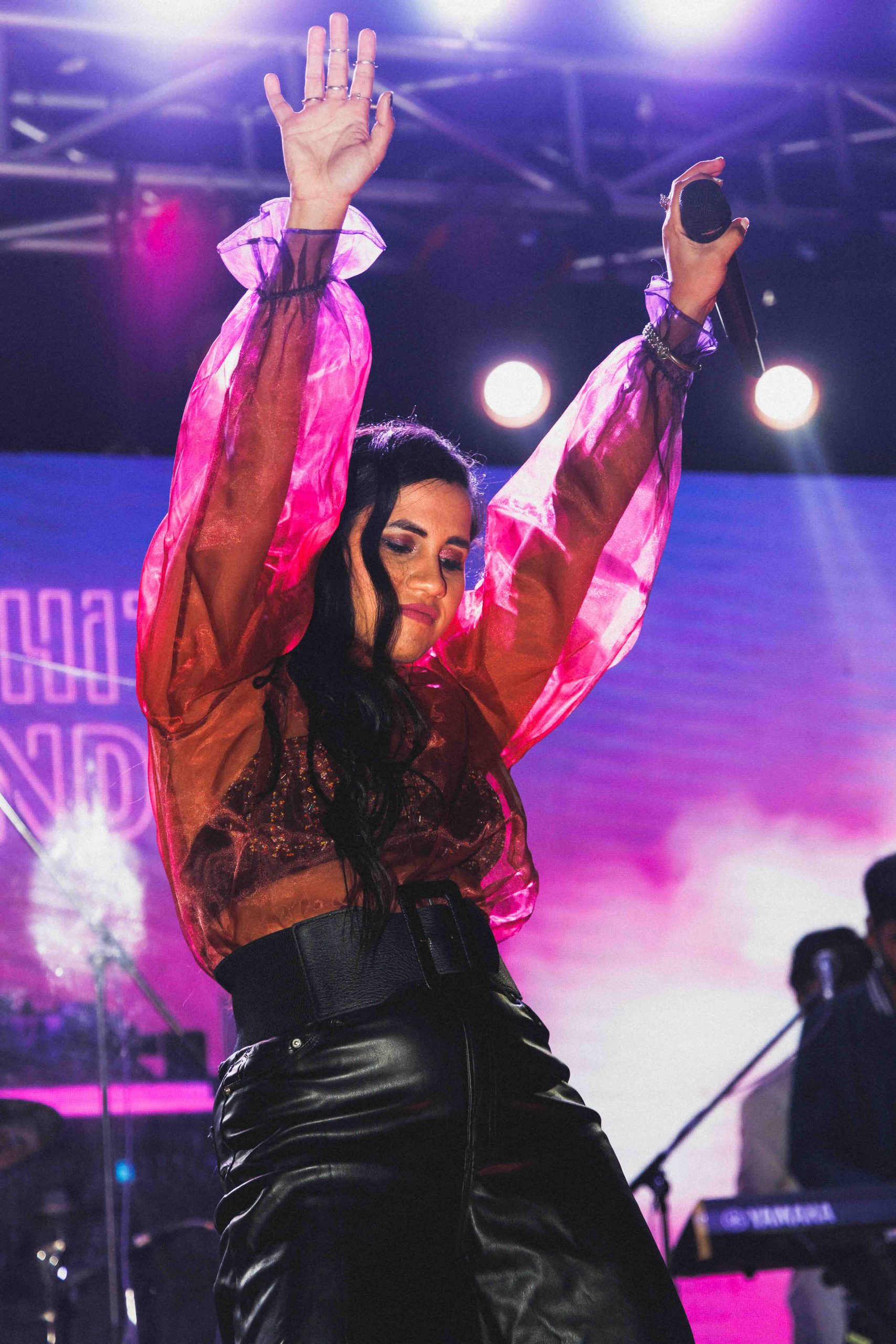 Singer with arms raised under magenta stage light