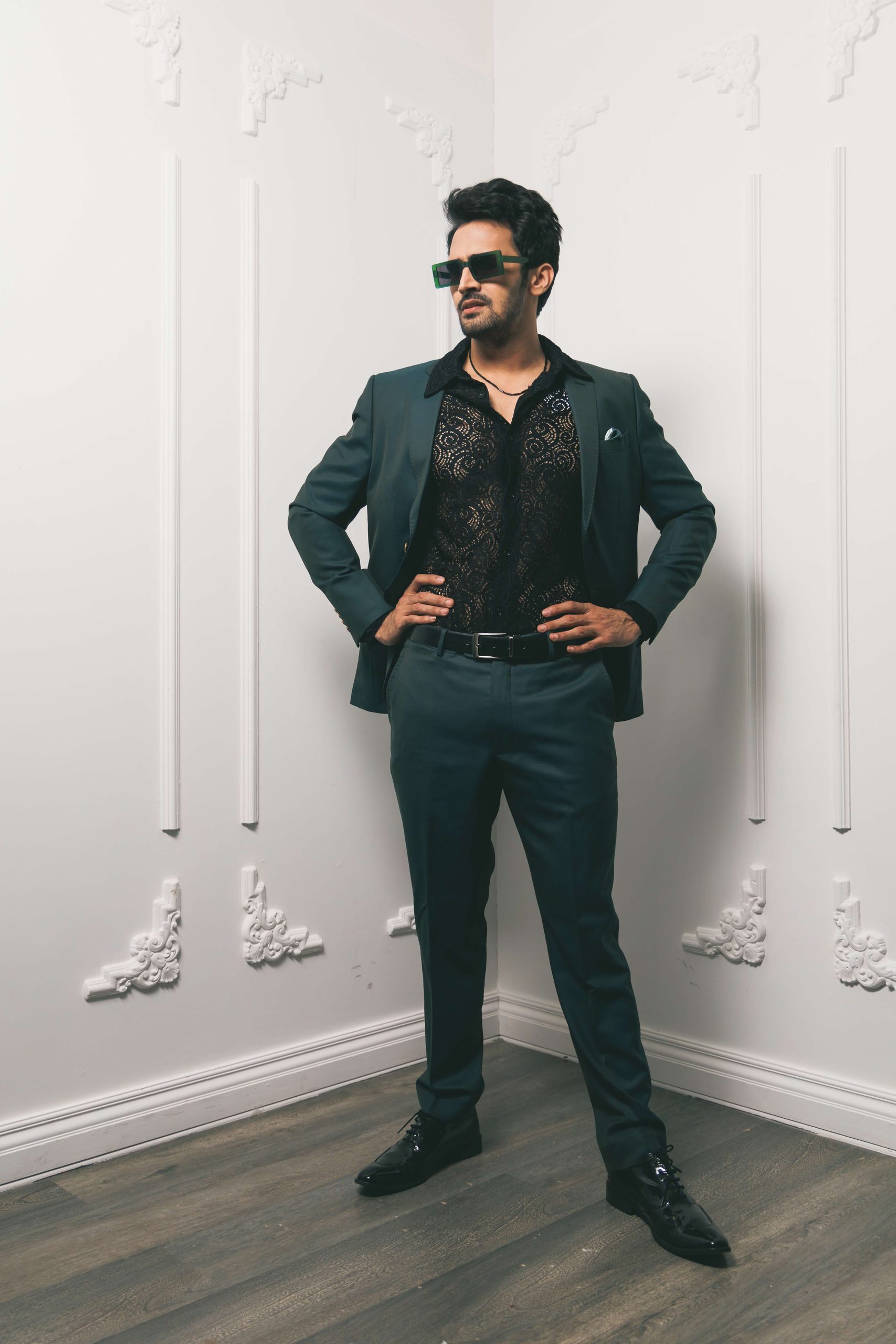Model in a black shirt and blazer against a white panelled wall